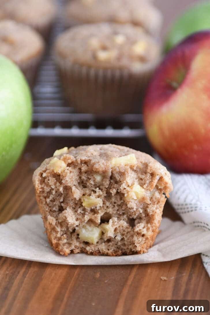 Spiced Apple Cinnamon Treats 11 A half-eaten apple cinnamon muffin showcasing the generous apple pieces within, resting on its paper liner.