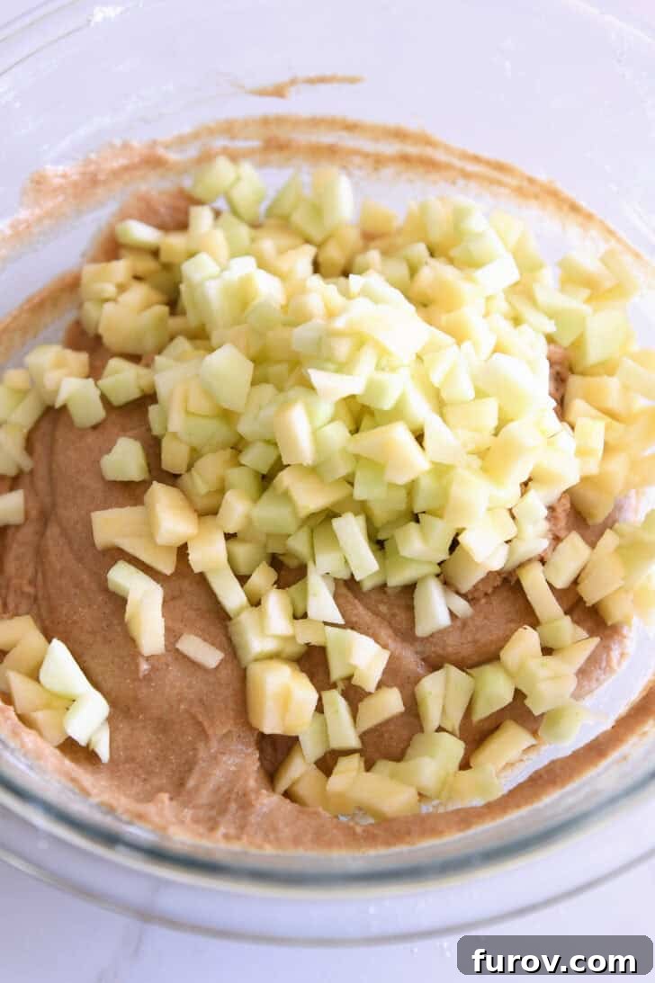 Spiced Apple Cinnamon Treats 6 Freshly chopped apple pieces scattered on top of the muffin batter in a glass bowl, ready for the final stir.