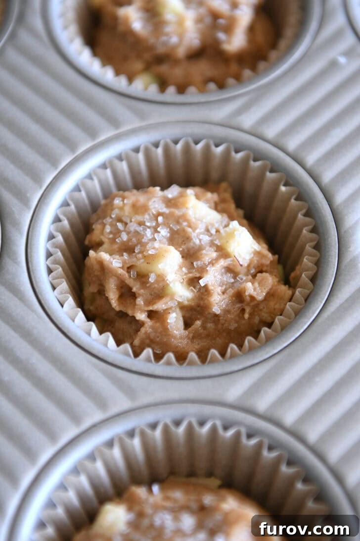 Spiced Apple Cinnamon Treats 7 Unbaked apple muffin batter generously spooned into a paper-lined muffin tin, ready for the oven.
