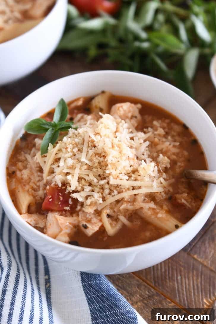 A vibrant bowl of Instant Pot Chicken Parmesan Soup, brimming with cooked pasta, tender chicken, rich tomatoes, and aromatic seasonings, beautifully topped with golden buttered breadcrumbs and grated Parmesan cheese.