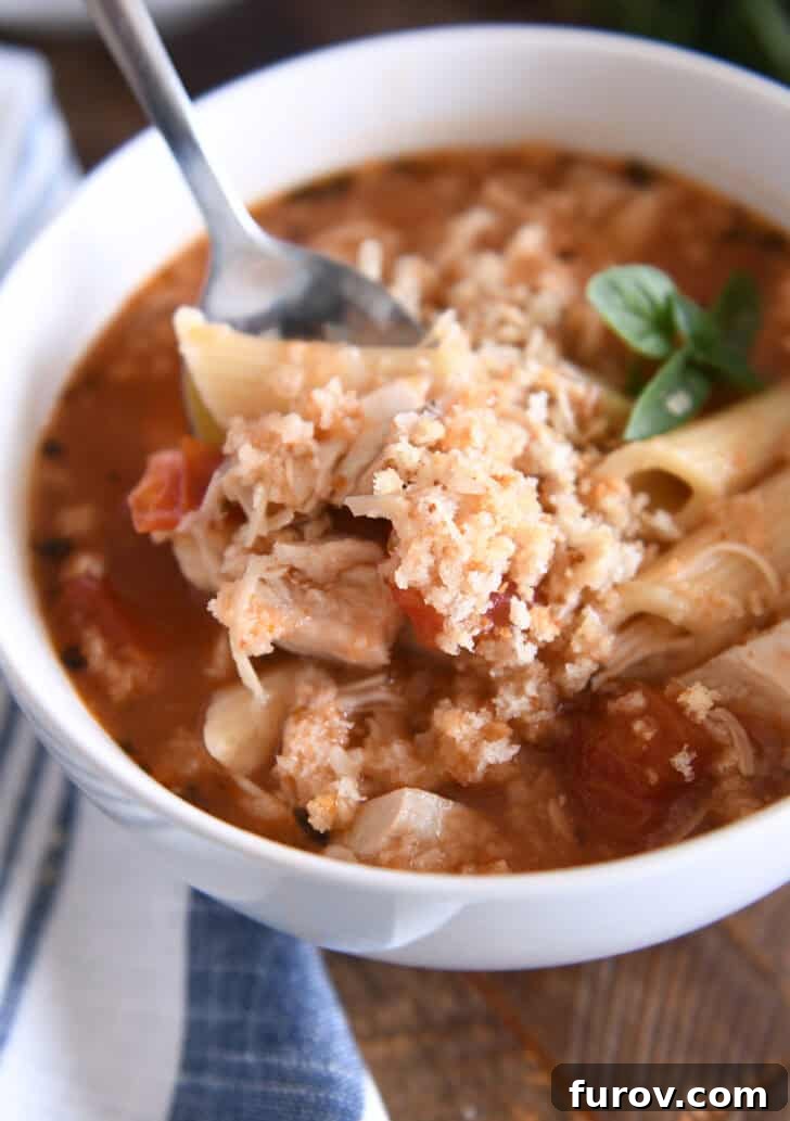A tempting bowl of Instant Pot Chicken Parmesan Soup, complete with tender pasta, flavorful chicken, rich tomatoes, and seasonings, lavishly garnished with buttered breadcrumbs and grated Parmesan for a delightful finish.