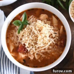 Top down view of chicken parmesan soup with cooked pasta, chicken, tomatoes, and seasonings in white bowl topped with buttered bread crumbs with Parmesan.