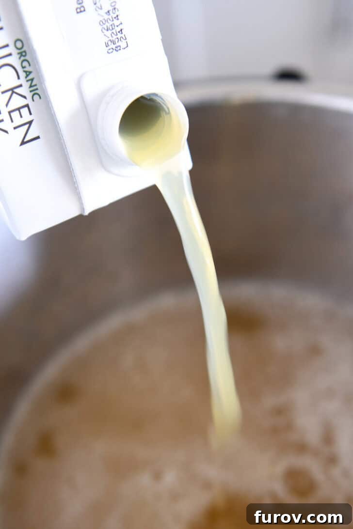 Pouring rich chicken broth into the Instant Pot, preparing the liquid foundation for the Chicken Parmesan Soup.