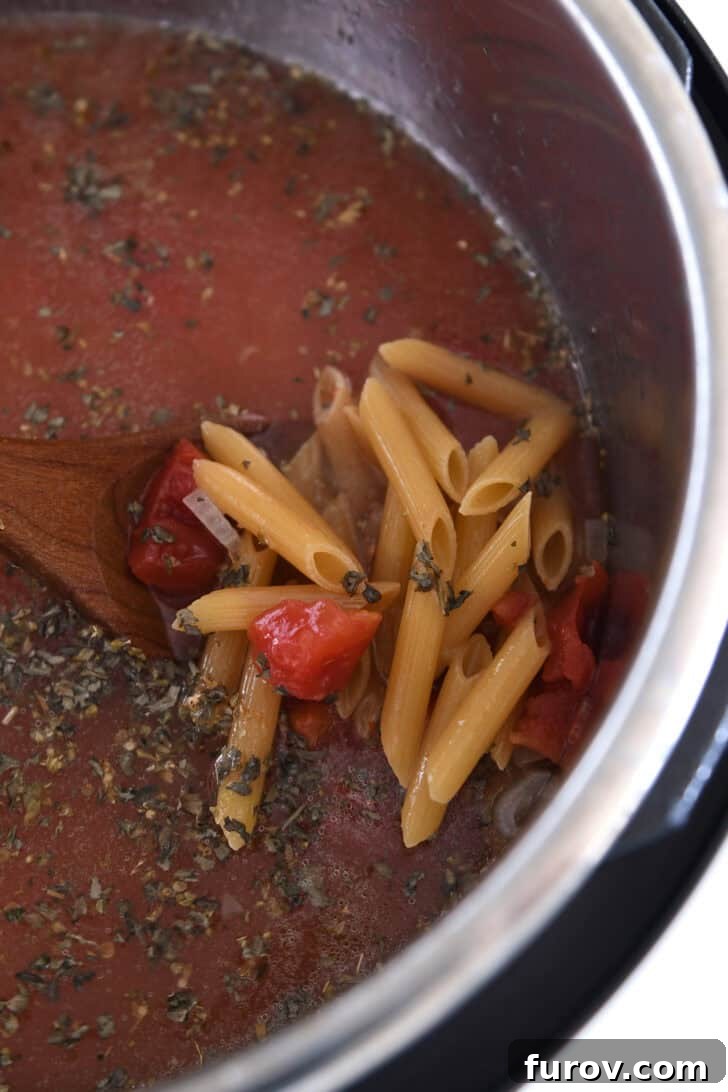 Uncooked penne pasta, vibrant diced tomatoes, savory broth, and a blend of seasonings neatly arranged in the Instant Pot, ready for pressure cooking into a delicious soup.