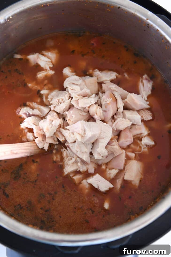 Cooked chicken blending seamlessly into the Instant Pot with a rich broth, tomatoes, and seasonings, ready for the final touches.