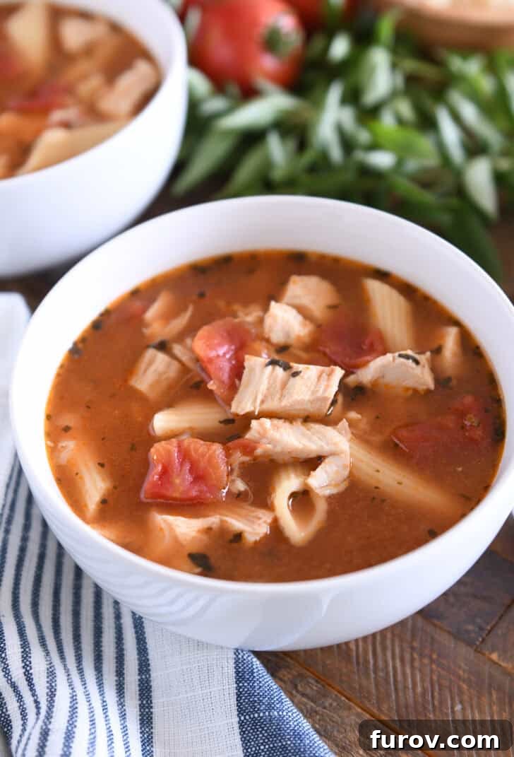A pristine white bowl filled with comforting chicken parmesan soup, showcasing tender pasta, succulent chicken, rich tomatoes, and aromatic seasonings, ready for its topping.