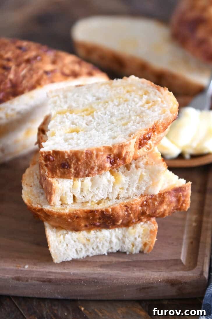 Four half slices of golden, cheesy peasant bread arranged beautifully on a dark wood cutting board, showcasing its fluffy interior.