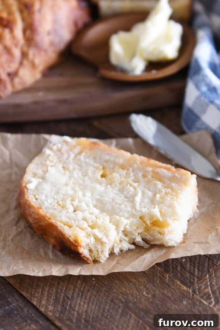 Close-up of a bite taken out of a slice of cheesy peasant bread on brown parchment paper, showing the airy texture and melted cheese.