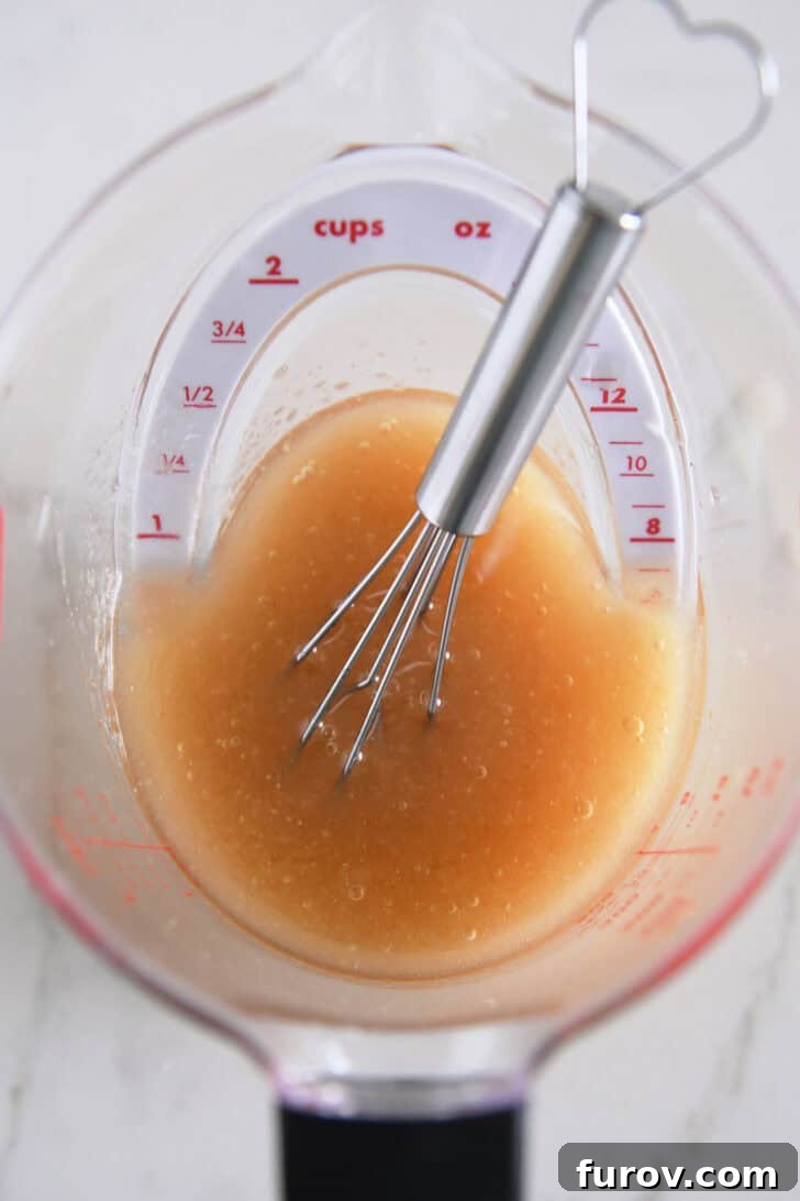 Small whisk in liquid measuring cup with vinaigrette.