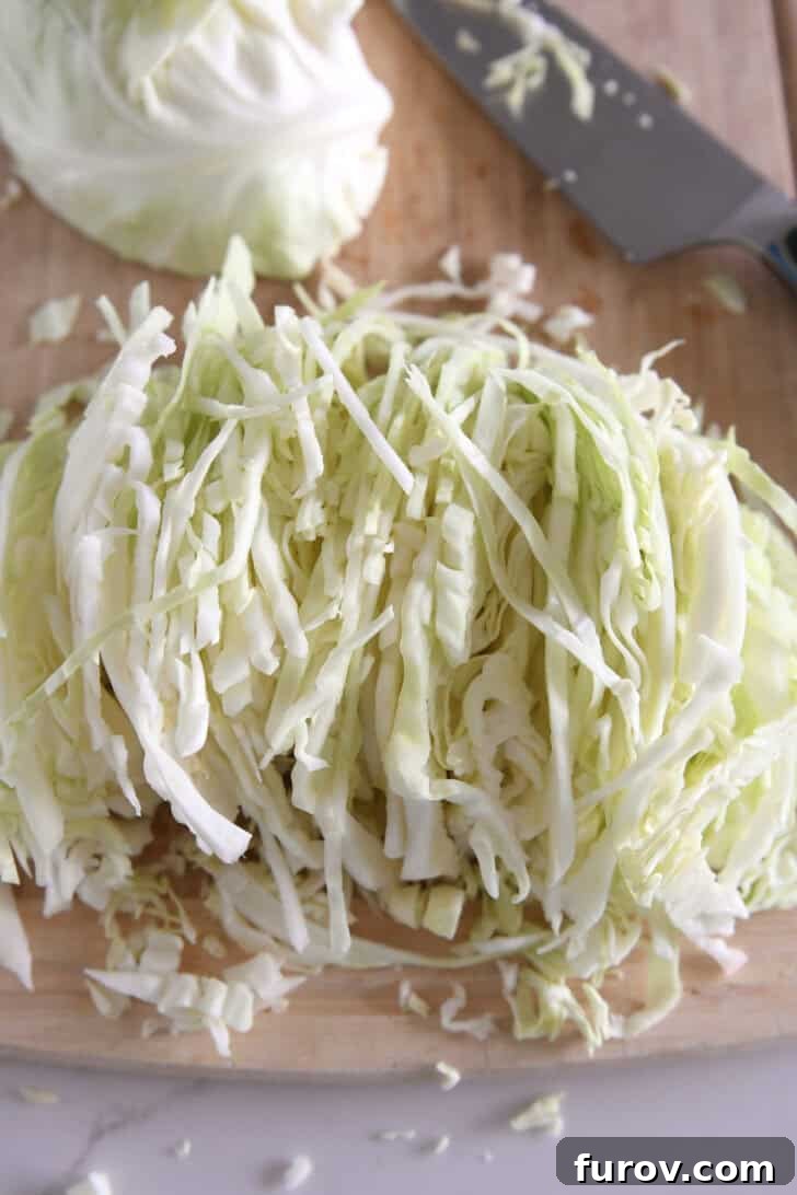 Thin slices of green cabbage on wood cutting board.