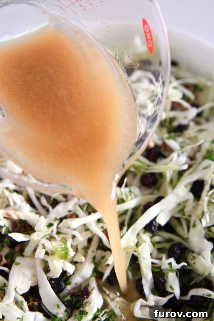 Pouring vinaigrette from liquid measuring cup onto thinly sliced cabbage salad.