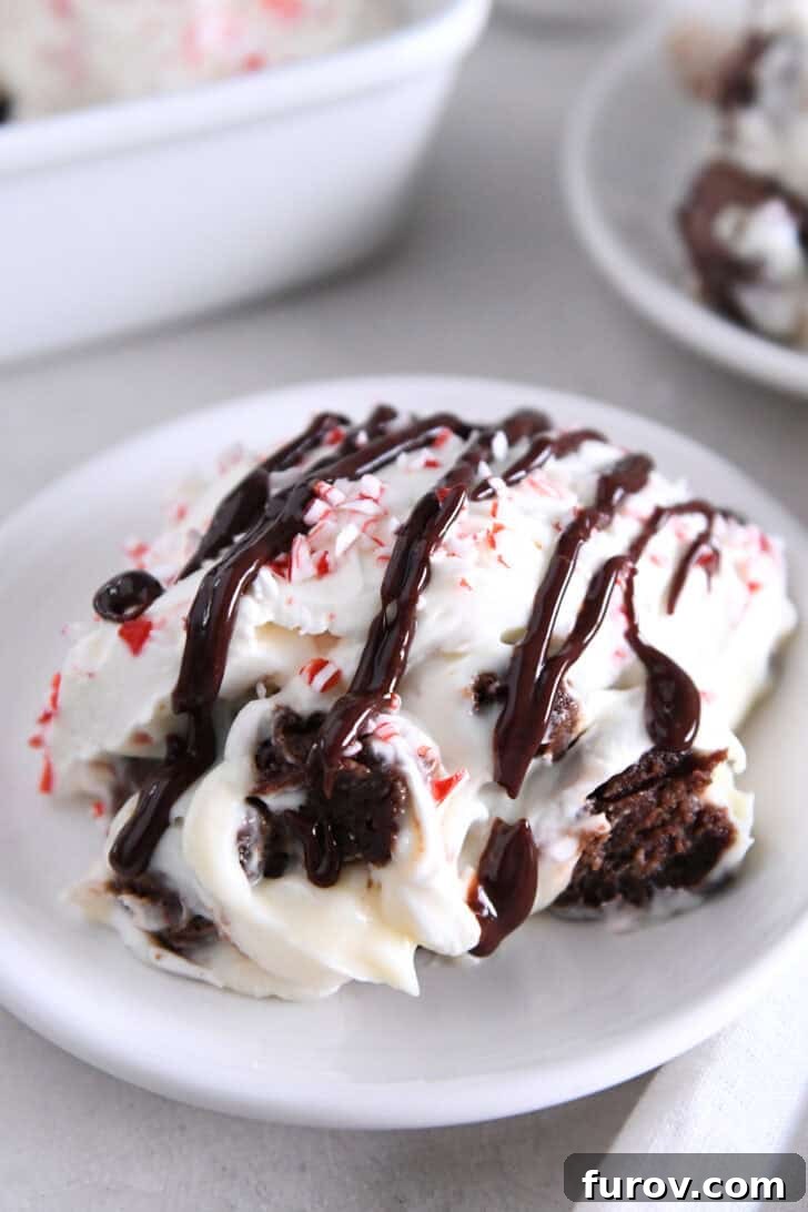 Serving of brownie peppermint bark pudding trifle on white plate drizzled with hot fudge sauce.