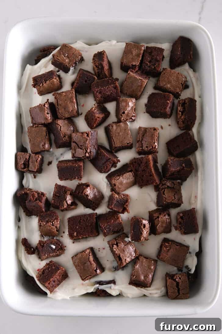 Brownie cubes on top of peppermint cream cheese layer in white dish.