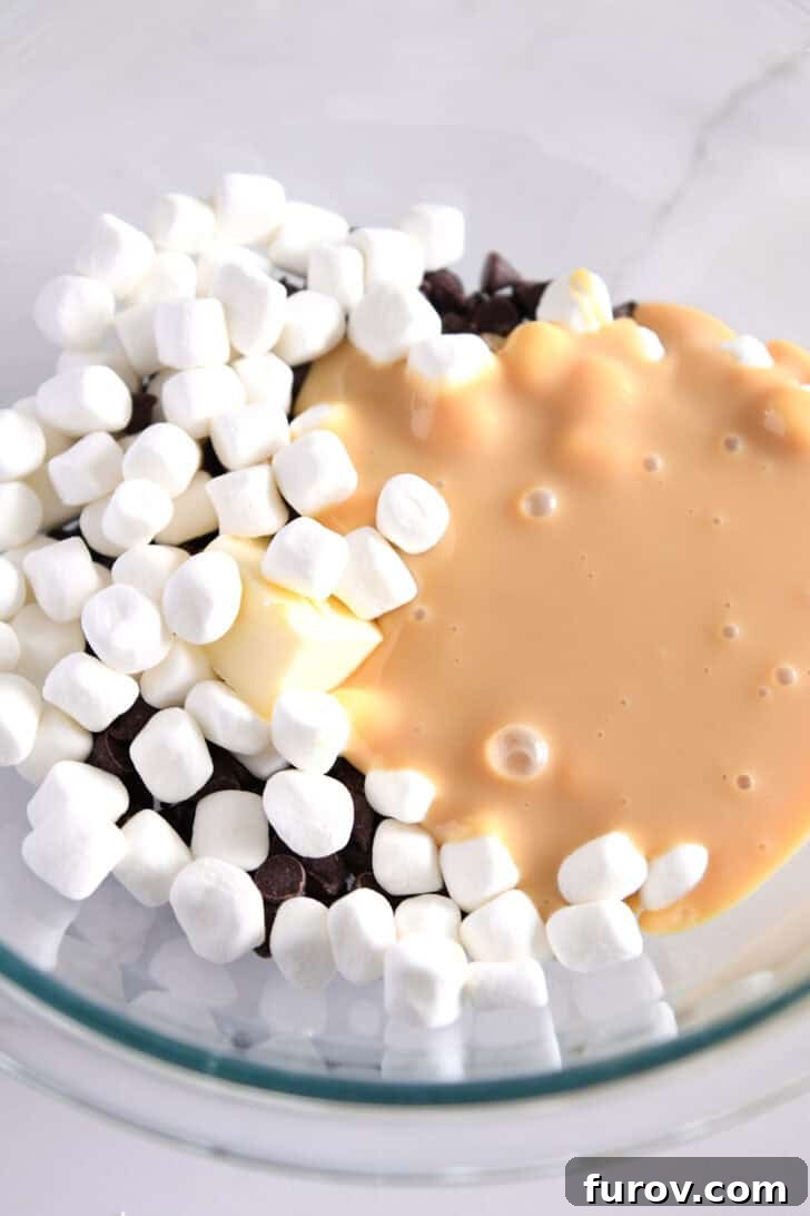 Candy Cane Swirl Fudge 3 A glass bowl filled with the base ingredients for fudge, including mini marshmallows, sweetened condensed milk, a pat of butter, and a generous amount of semisweet chocolate chips, ready for microwaving.