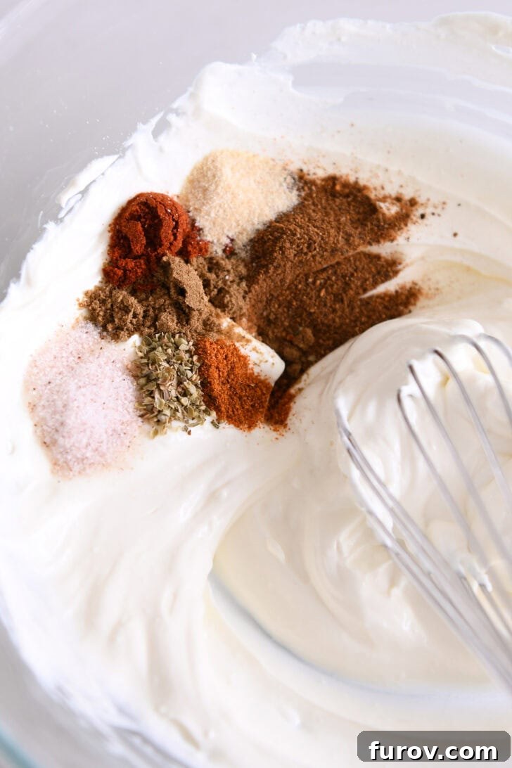 A bowl containing a smooth, creamy mixture of sour cream and perfectly softened cream cheese, infused with aromatic spices like cumin, chili powder, garlic powder, onion powder, oregano, and salt, ready for the next step.