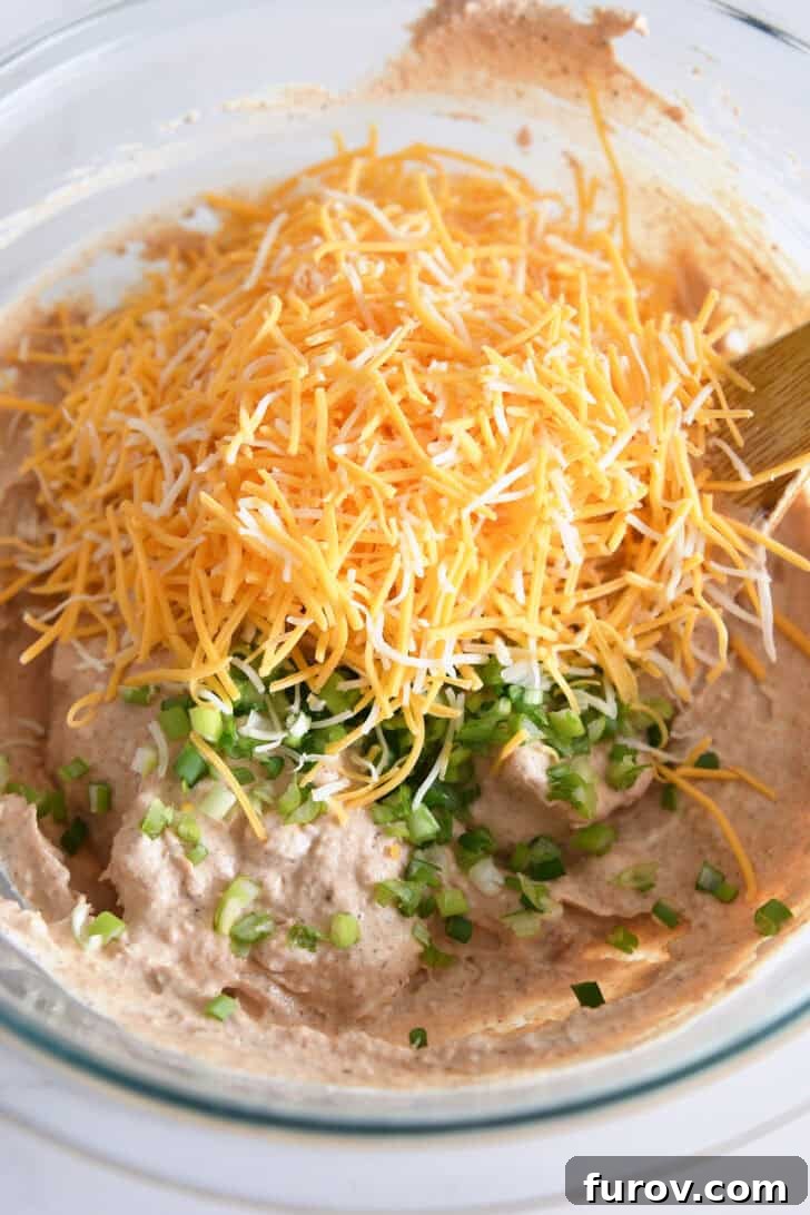 The creamy refried bean mixture in a bowl, now beautifully combined with a generous amount of shredded cheese and freshly chopped green onions, poised for its final baking stage.