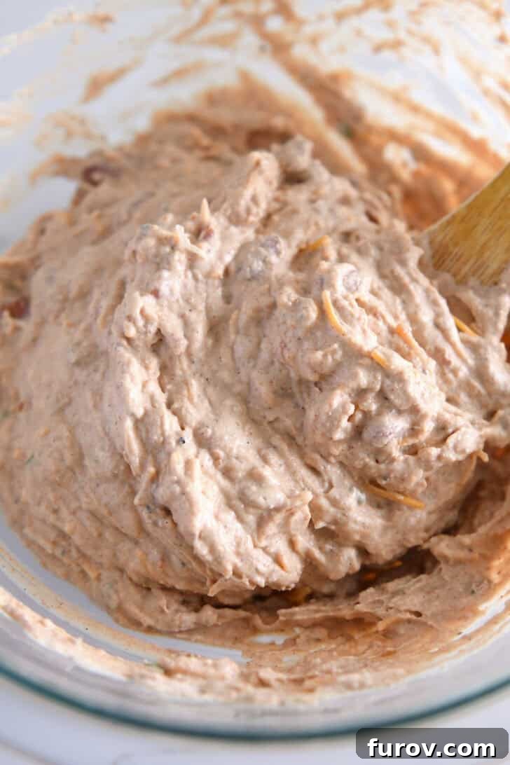 A close-up view of all the key ingredients—refried beans, sour cream, cream cheese, and various spices—perfectly mixed together in a clear glass bowl, showcasing the rich texture before baking.