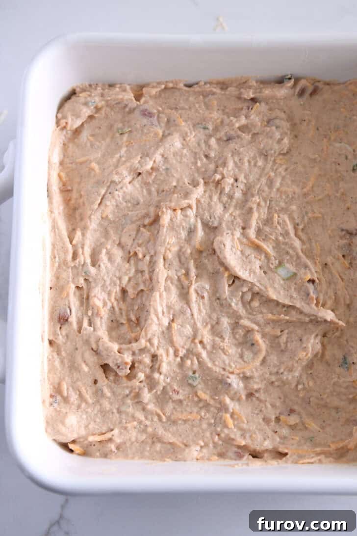 A pristine white square baking pan filled with the smooth, creamy refried bean dip mixture, spread evenly and ready for its cheesy topping.