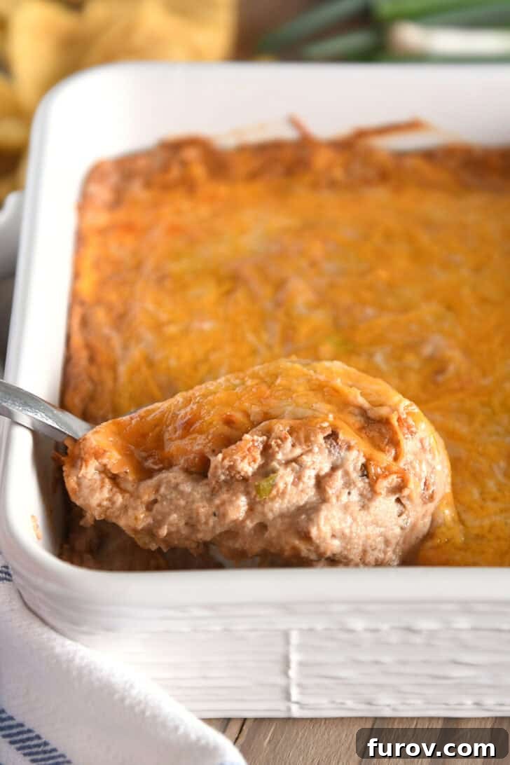 A serving spoon gracefully scooping a generous portion of warm, gooey bean dip from a white square baking dish, showcasing its perfect melted cheese topping and inviting texture.