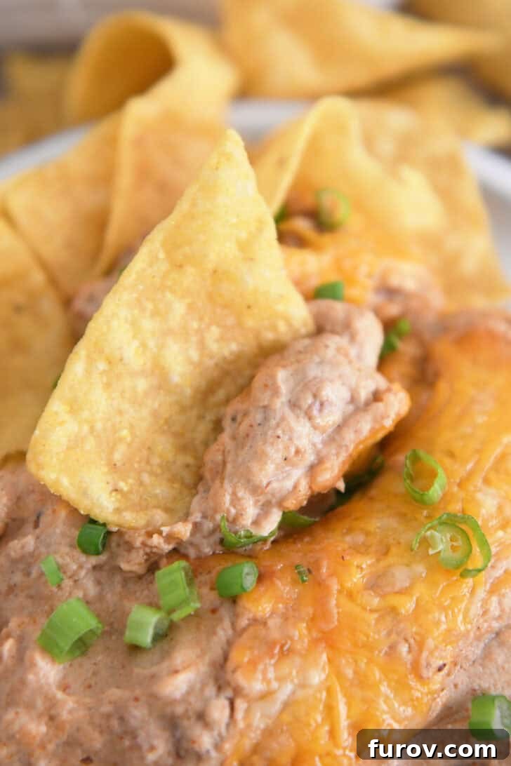 A perfectly loaded tortilla chip, adorned with a delightful scoop of warm bean dip, showing off the melted cheese and flecks of green onions, ready for a bite.