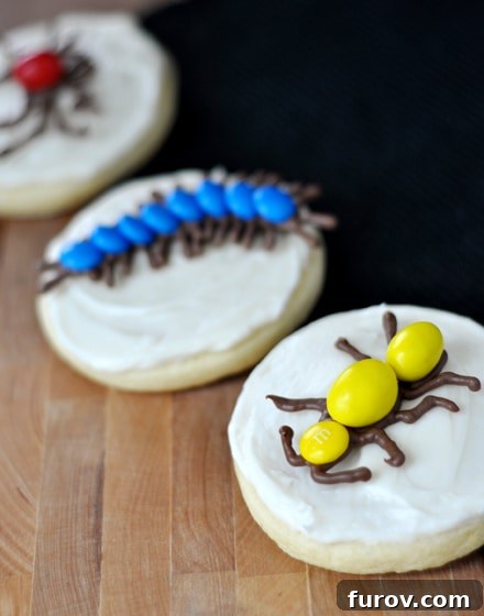Sugar cookies with white frosting and intricate chocolate bug designs on top.