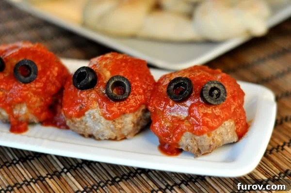 Three meatballs with red sauce and olive eyes lined up on a small rectangular white platter, ready to be served as spooky Halloween food.