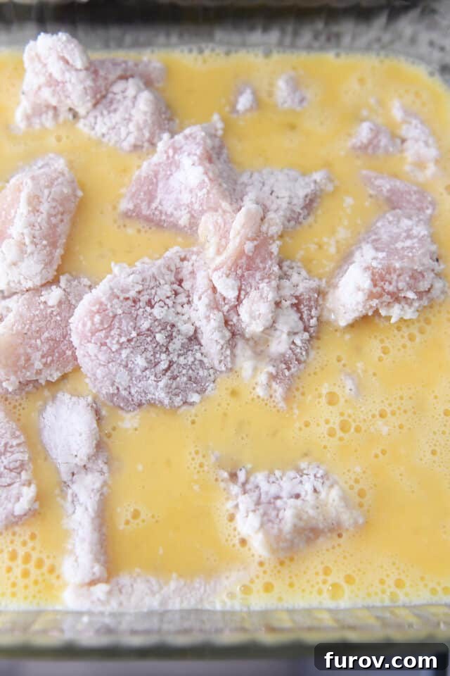 Tangy Honey Glazed Chicken 6 Cornstarch-coated chicken pieces soaking in a bowl of whisked egg mixture, ready for frying.