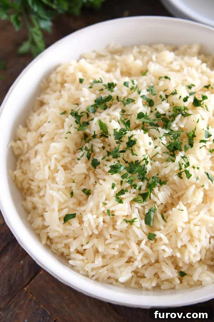 A pristine white bowl filled with perfectly fluffy garlic butter rice, garnished with fresh, vibrant green parsley.
