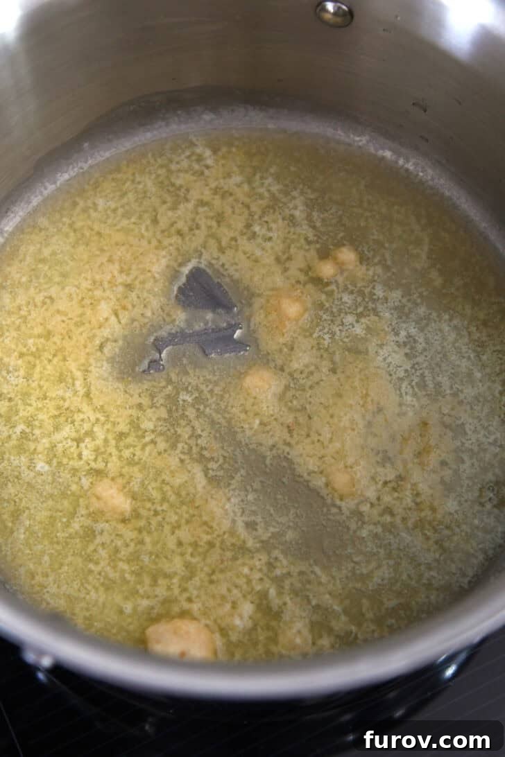 Golden butter and finely minced garlic simmering gently in a gleaming stainless steel pot, releasing a fragrant aroma.