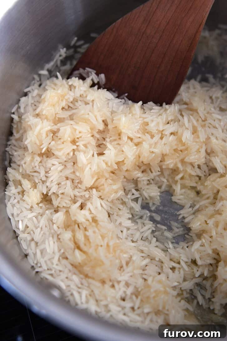 White rice grains actively cooking, being stirred in melted butter within a stainless steel pot, achieving an even coating.