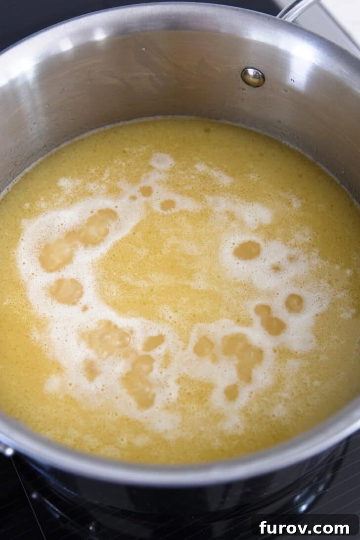 Chicken broth gently simmering with rice in a stainless steel pan, indicating the cooking process is underway.