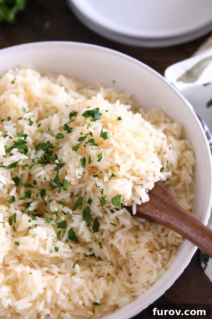 A wooden spoon delicately scooping fluffy white rice, adorned with fresh green parsley, from a serving bowl.