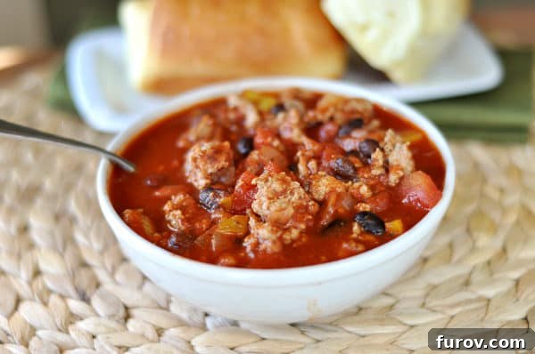 Comforting Turkey and Bean Chili 2 White bowl with black bean turkey chili and a plate of bread in the background.