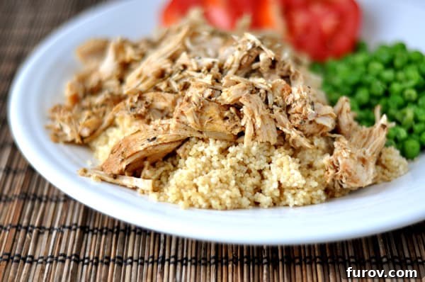 White plate with shredded pork, cooked couscous, peas, and sliced tomatoes.