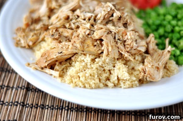 White plate with shredded pork atop a bed of cooked couscous and green peas on the side.