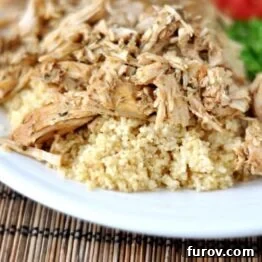 White plate with shredded pork atop a bed of cooked couscous and green peas on the side.