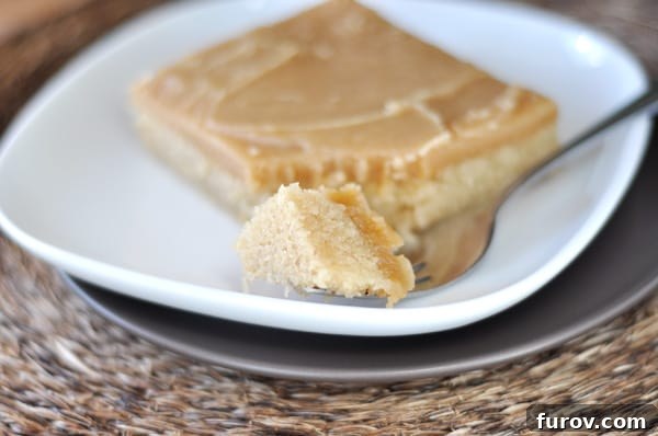 Texas Sized Peanut Butter Bliss Cake 2 A generous slice of Peanut Butter Texas Sheet Cake on a pristine white plate, with a fork gently scooping a bite, showcasing its luscious frosting and moist interior.