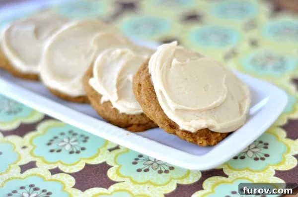 A white platter with four frosted pumpkin cookies, showcasing their fluffy texture and golden caramel frosting.