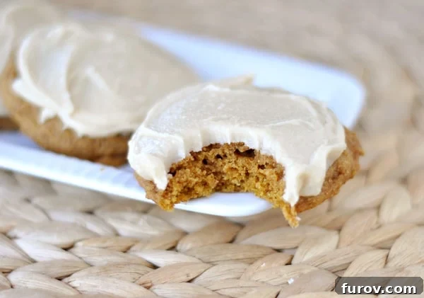 A close-up of a frosted pumpkin cookie with a bite taken out, revealing its soft interior and the thick caramel frosting.