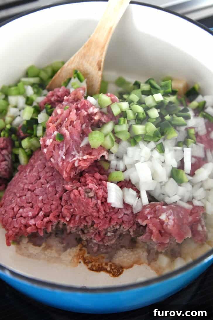 Cast iron pot with ground beef, ground pork, jalapenos, bell peppers, onions and garlic.
