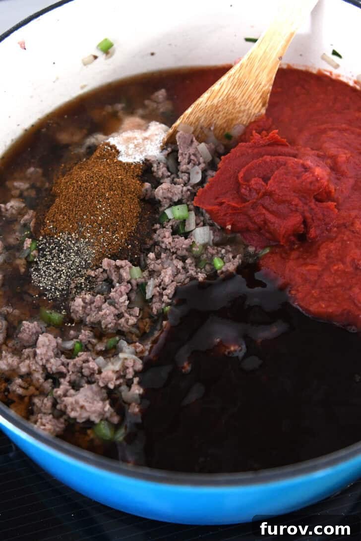 Cast iron pot with ground beef, tomato paste, crushed tomatoes, BBQ sauce, chili powder, and salt.