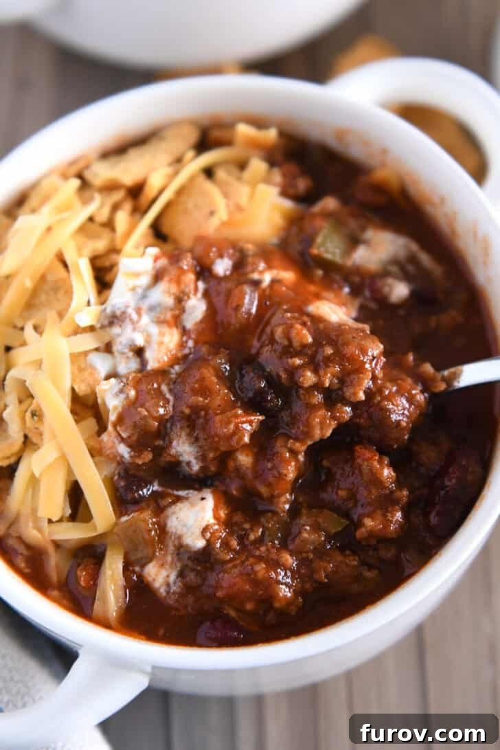 Top down view of spoon scooping bite of beef and bean tomato Southern chili.