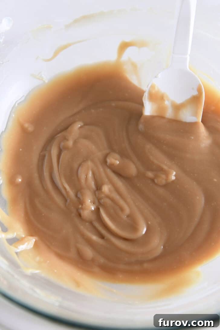 Caramel-Soaked Pumpkin Poke Cake with Whipped Caramel Topping 11 Glass bowl filled with a smooth mixture of caramel sauce and cream cheese, forming the base for the whipped frosting.