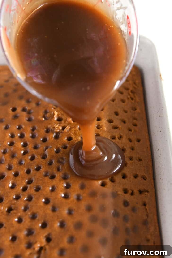 Caramel-Soaked Pumpkin Poke Cake with Whipped Caramel Topping 15 Warm caramel sauce being poured generously over the top of a poked pumpkin cake in a baking pan.