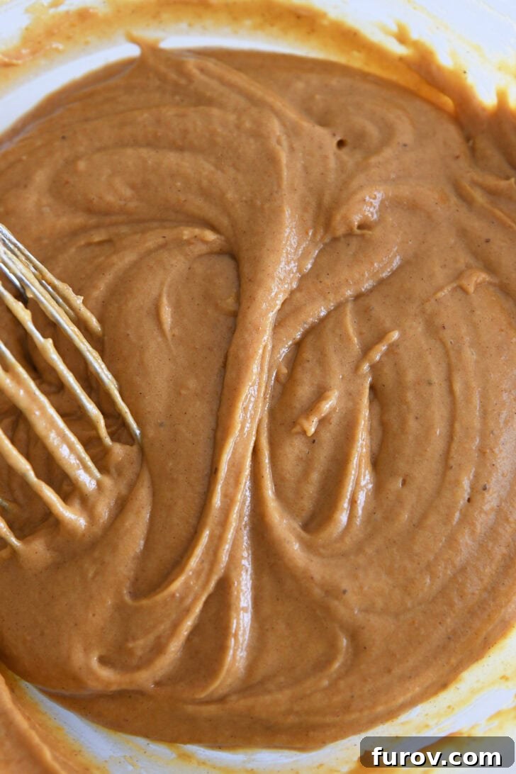 Caramel-Soaked Pumpkin Poke Cake with Whipped Caramel Topping 5 Pumpkin cake batter in a glass bowl, perfectly mixed with a whisk, showing a smooth and consistent texture.
