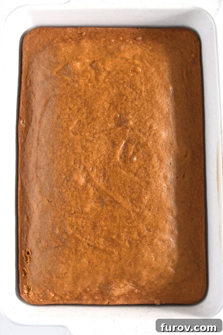 Caramel-Soaked Pumpkin Poke Cake with Whipped Caramel Topping 6 Freshly baked pumpkin cake cooling in a white 9x13-inch pan, ready for the caramel sauce.