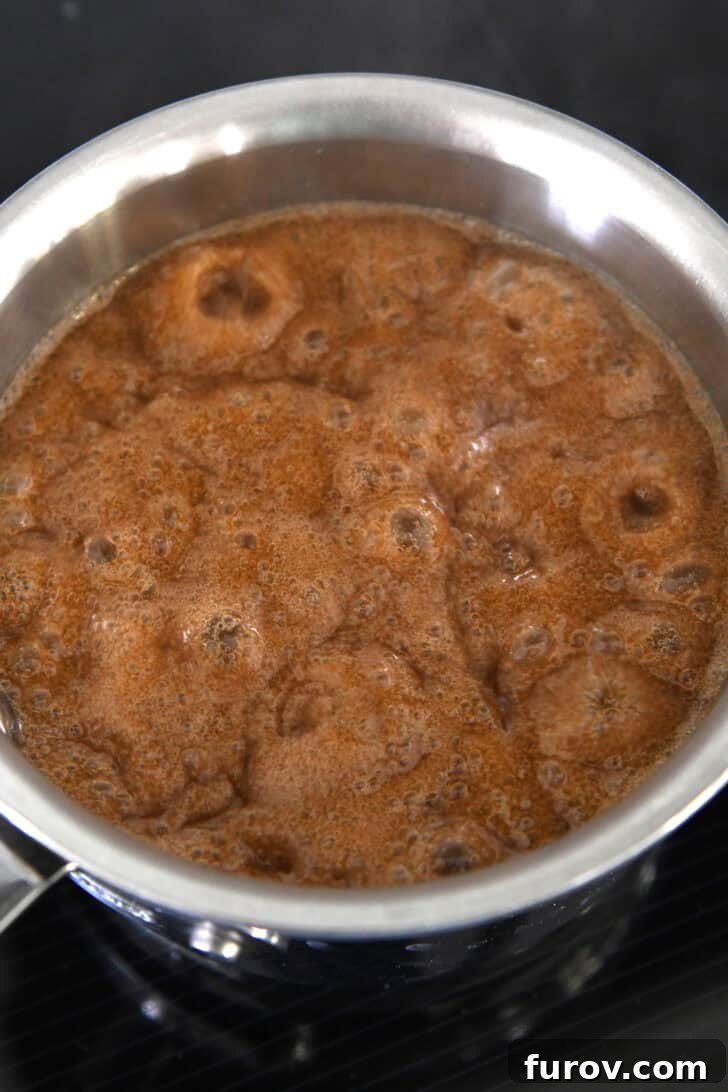 Caramel-Soaked Pumpkin Poke Cake with Whipped Caramel Topping 8 Small pan of bubbling caramel sauce cooking on an induction stove, indicating it's reaching the perfect consistency.