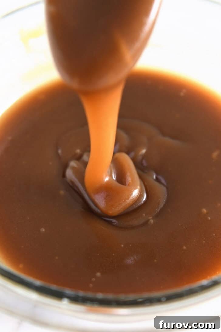Caramel-Soaked Pumpkin Poke Cake with Whipped Caramel Topping 9 Thick, rich caramel sauce being drizzled into a glass bowl with a spoon, highlighting its perfect consistency.