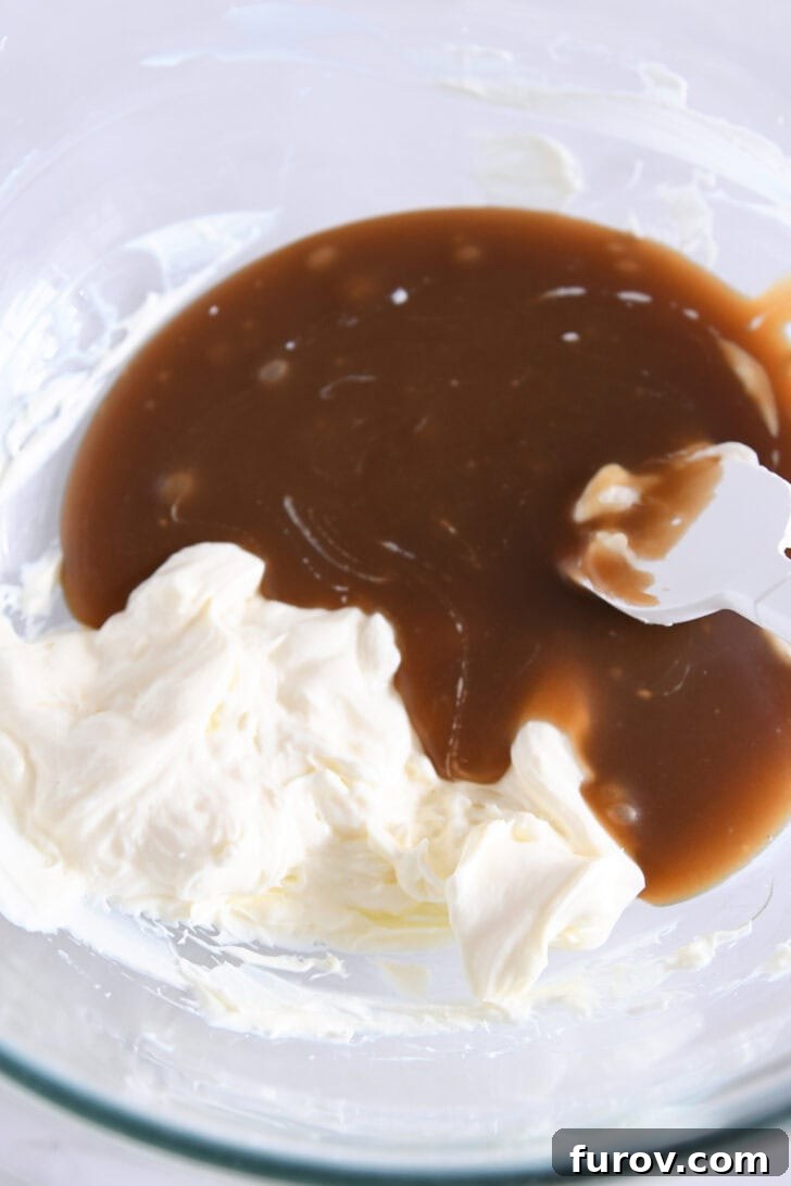 Caramel-Soaked Pumpkin Poke Cake with Whipped Caramel Topping 10 Glass bowl showing whipped cream cheese and the addition of cooled caramel sauce, ready to be combined for the frosting.