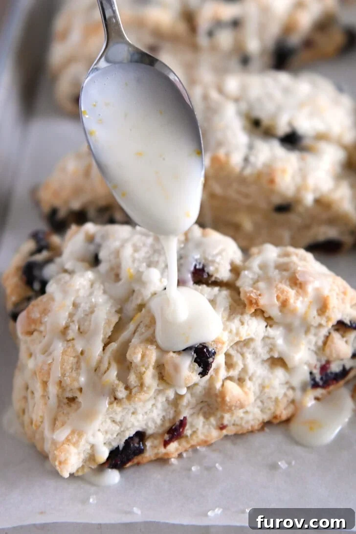 Sunburst Cranberry White Chocolate Scones 13 Spoon drizzling orange creamy glaze over baked scone.